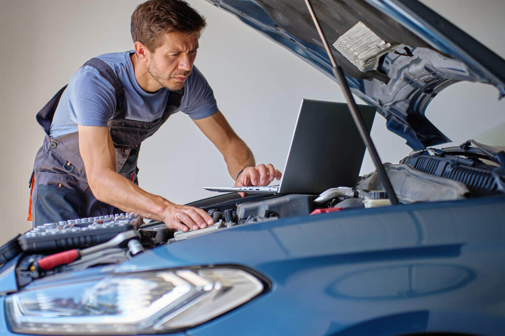 Ein Mechaniker überprüft den Motor eines Autos mit einem Laptop, um nach einem Unfall mit Fahrerflucht ein Gutachten zu erstellen